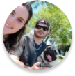 Uma mulher sorrindo ao lado de um homem segurando um buldog alemão branco com língua pra fora.